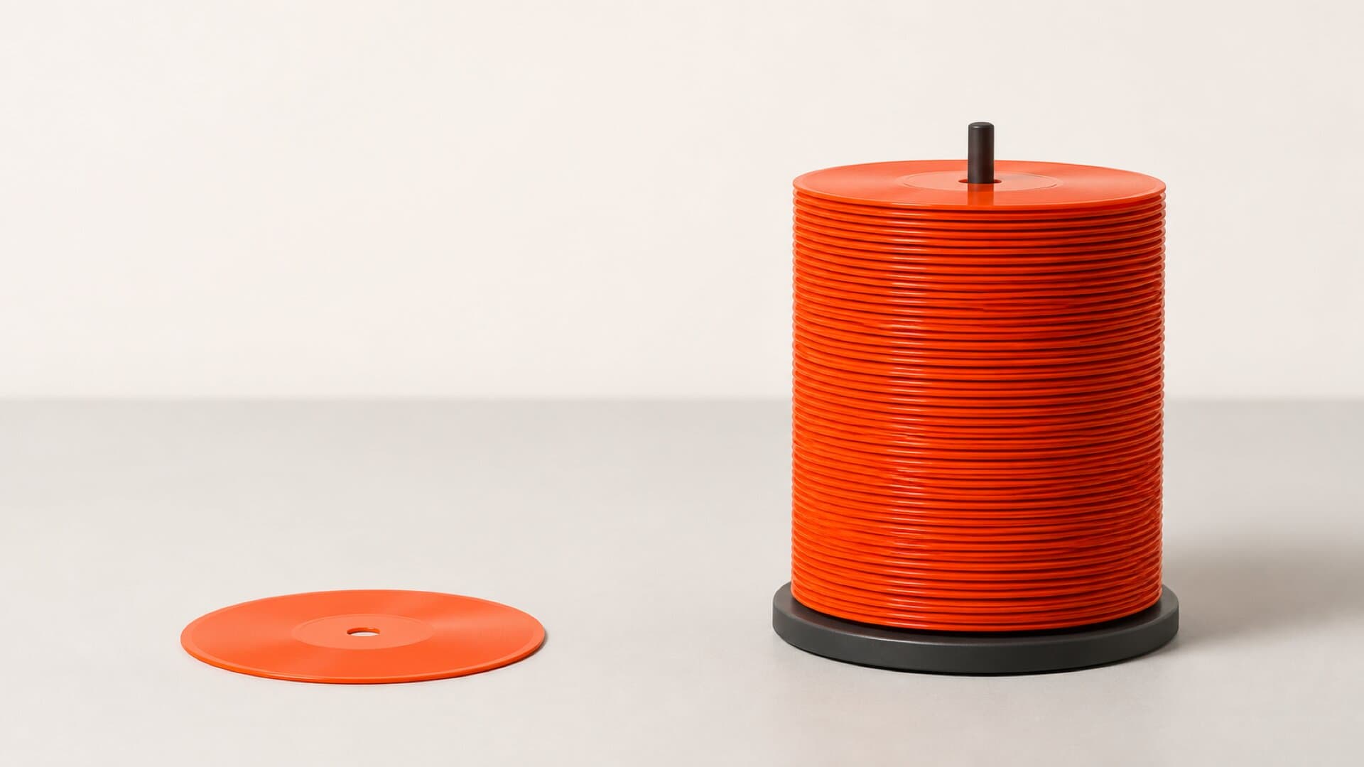 One orange vinyl record lying alone beside a tall spindle stacked with the same record, on a bright studio surface