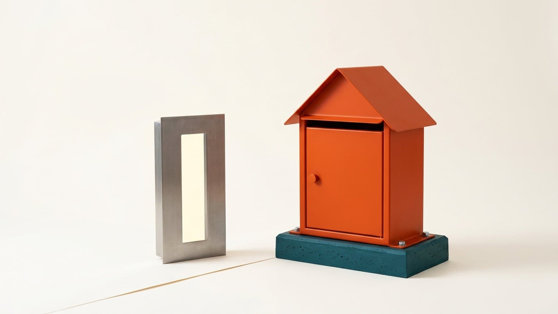 A hollow steel letter slot standing on nothing beside an orange steel mailbox bolted to a poured teal plinth