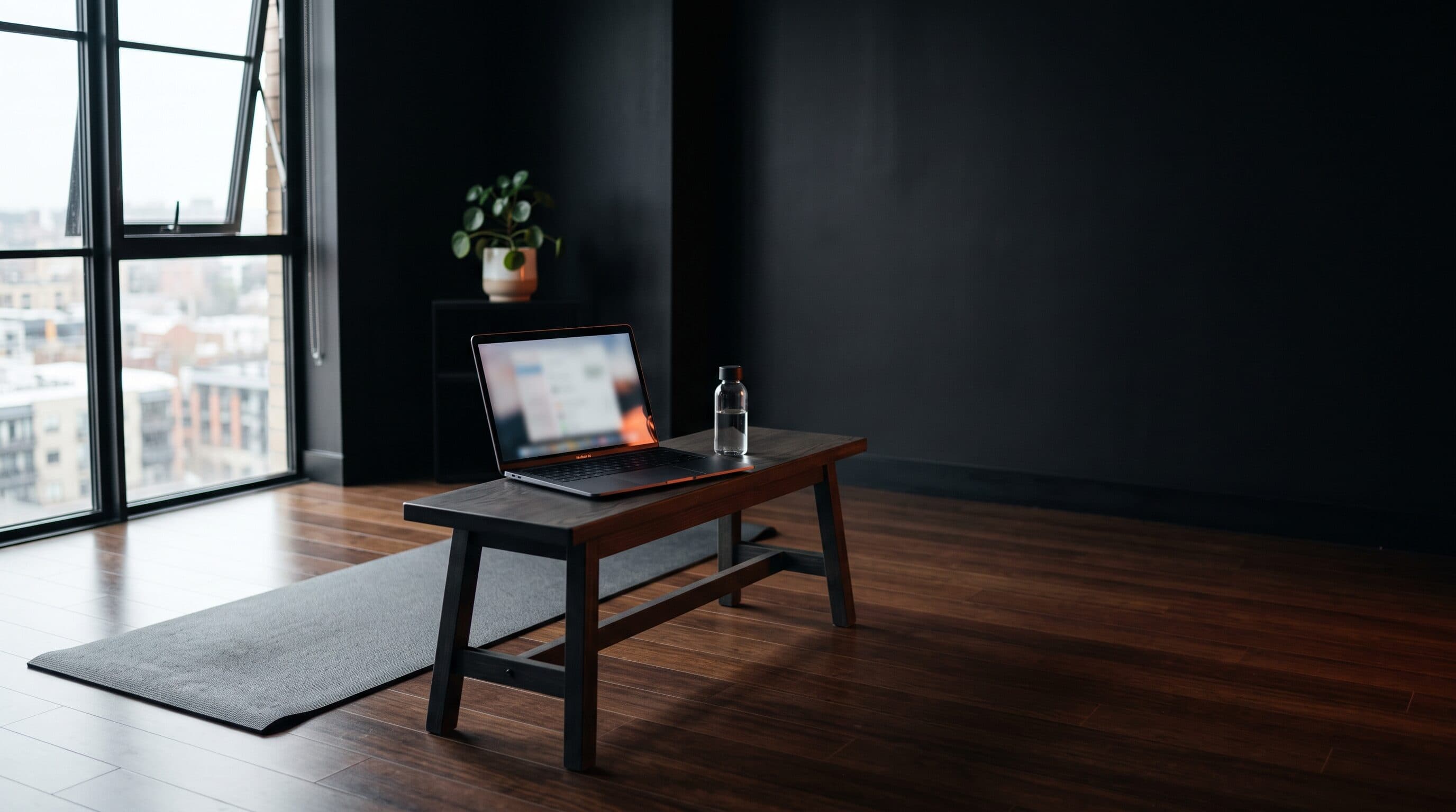 A minimal dark home living room set up for an at-home workout with a laptop and exercise mat, lit with a warm orange accent