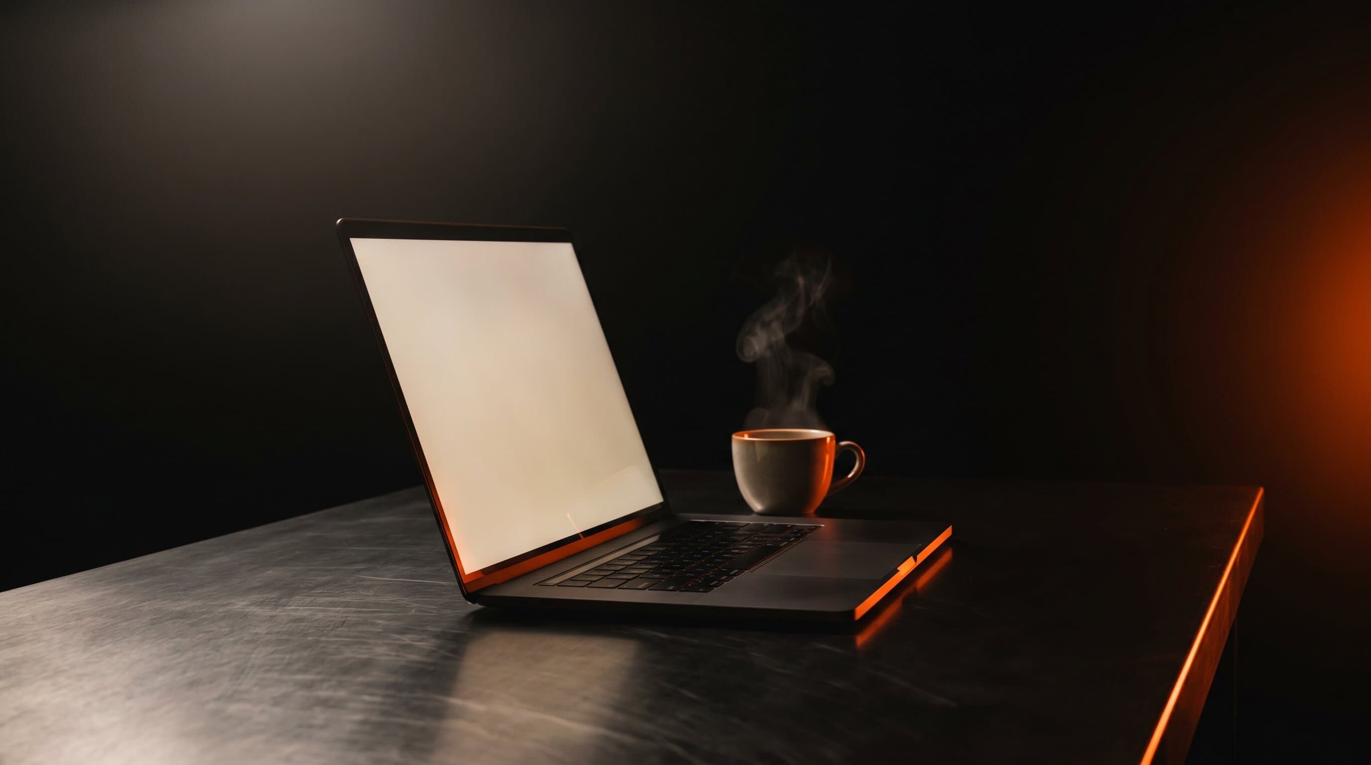 A laptop and coffee cup on a brushed steel desk in a dark home office, lit by warm orange rim light
